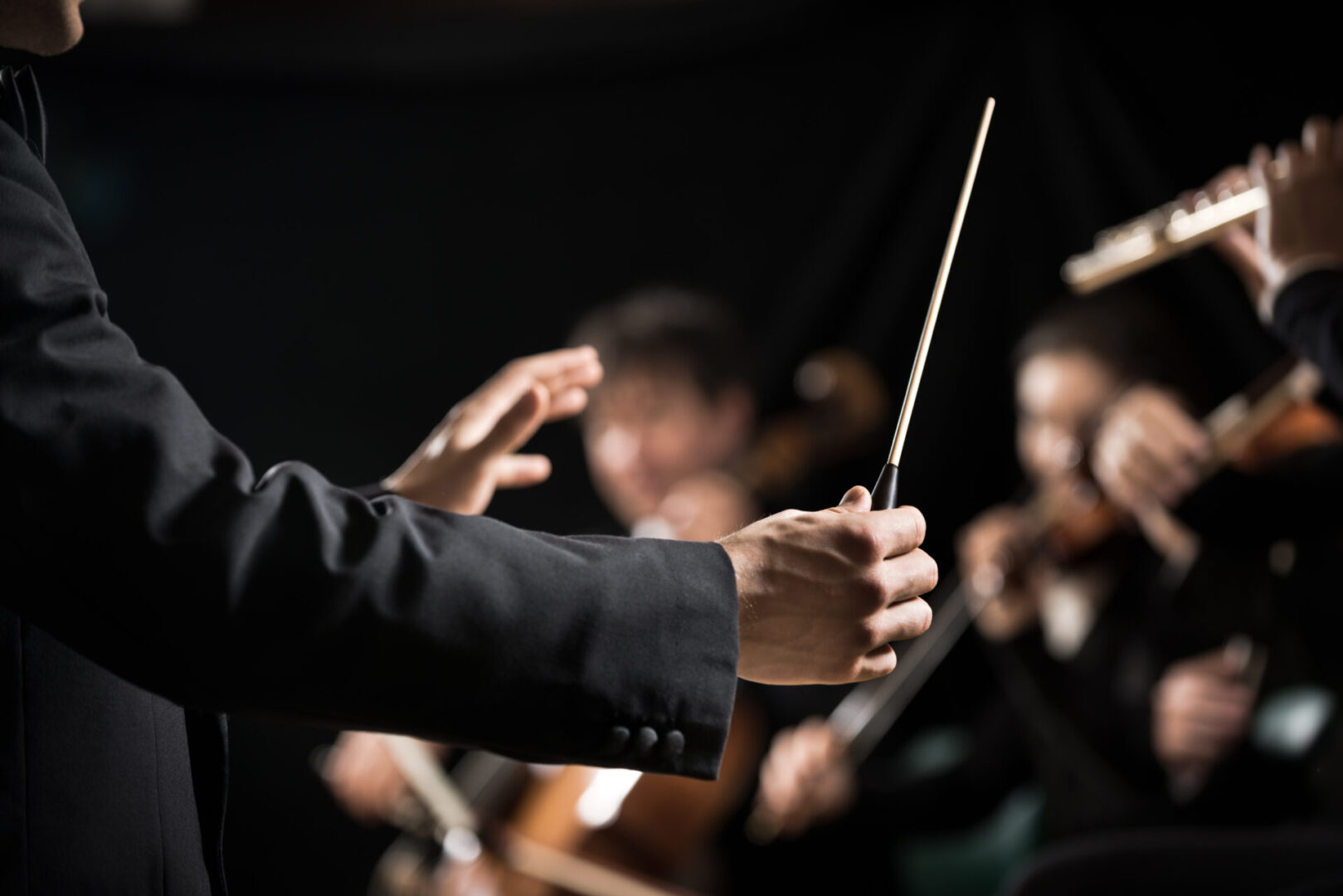 Conductor directing symphony orchestra with performers on background, hands close-up.